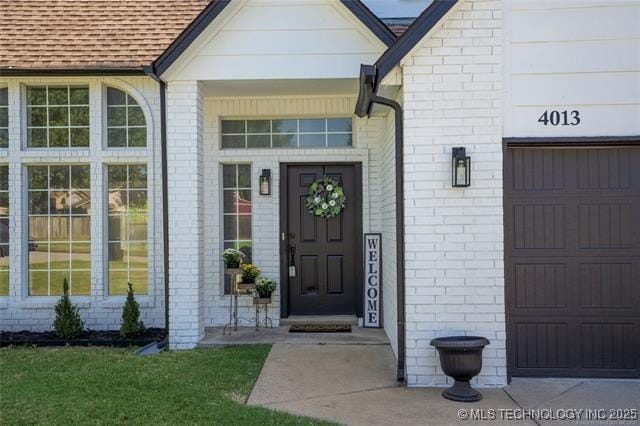doorway to property featuring a garage, brick siding, and a shingled roof