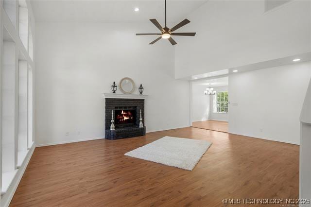 unfurnished living room featuring a brick fireplace, a chandelier, a ceiling fan, a towering ceiling, and wood finished floors