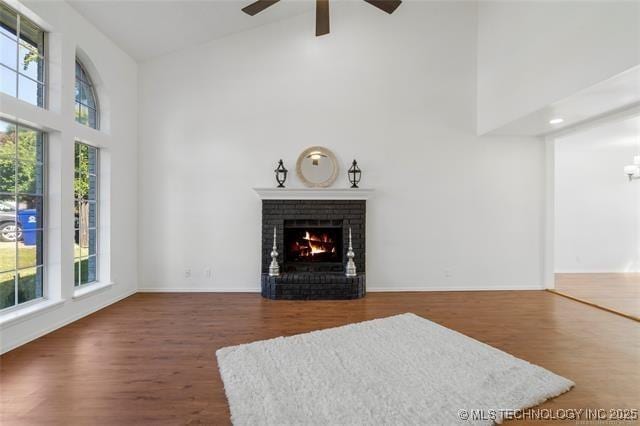 living room featuring high vaulted ceiling, ceiling fan, a brick fireplace, wood finished floors, and baseboards