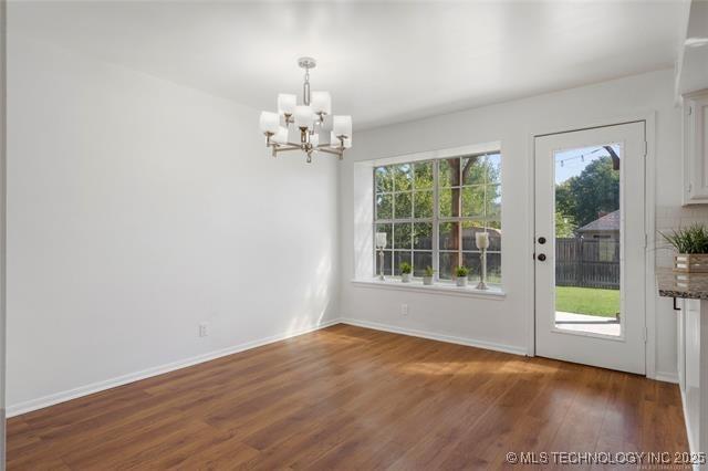 unfurnished dining area featuring a chandelier, dark wood-style floors, and baseboards