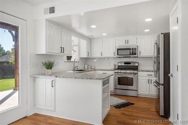 kitchen featuring appliances with stainless steel finishes, a peninsula, white cabinets, decorative backsplash, and wood finished floors