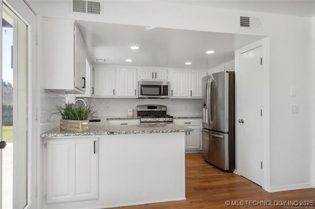 kitchen featuring stainless steel appliances, a peninsula, white cabinetry, tasteful backsplash, and recessed lighting