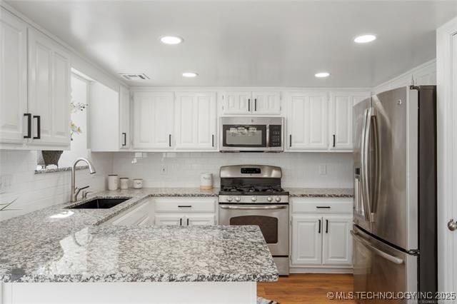 kitchen with stainless steel appliances, a sink, white cabinetry, a peninsula, and light stone countertops
