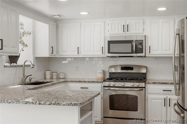kitchen featuring appliances with stainless steel finishes, a sink, white cabinets, light stone counters, and recessed lighting