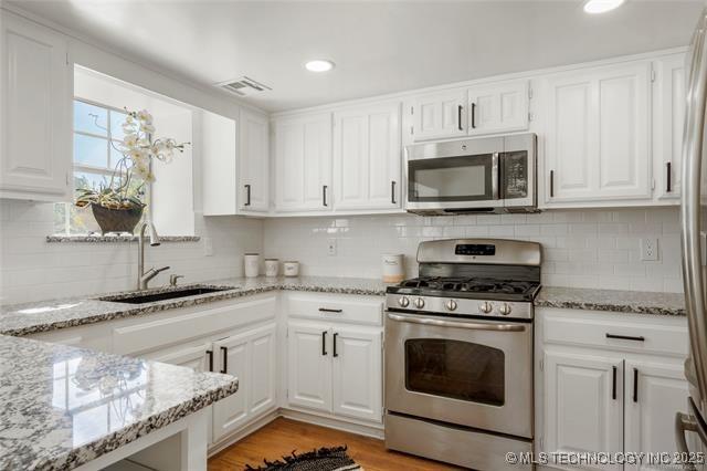 kitchen featuring appliances with stainless steel finishes, a sink, white cabinets, tasteful backsplash, and light stone countertops