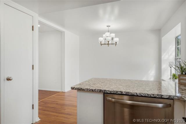 kitchen featuring dishwasher, light wood-style flooring, a chandelier, decorative light fixtures, and light stone counters