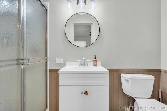 full bath featuring wainscoting, vanity, toilet, and a shower with door
