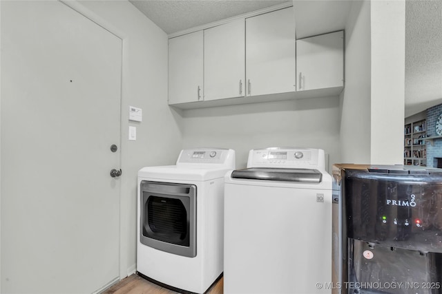 clothes washing area featuring washer and dryer, a textured ceiling, cabinet space, and light wood finished floors