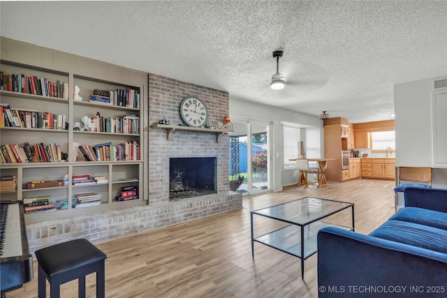 living area with light wood-type flooring, a ceiling fan, a fireplace, and a textured ceiling