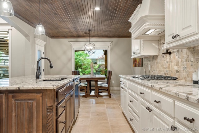 kitchen featuring a sink, premium range hood, backsplash, white cabinets, and light stone countertops