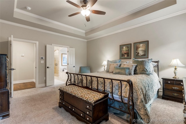carpeted bedroom featuring a tray ceiling, crown molding, baseboards, ensuite bath, and ceiling fan