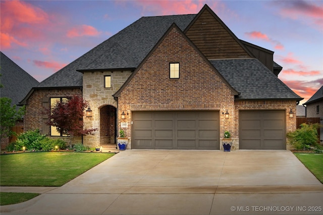 view of front of house with roof with shingles, stone siding, concrete driveway, a yard, and brick siding