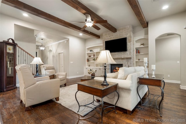 living room featuring baseboards, arched walkways, a ceiling fan, a fireplace, and dark wood-style flooring