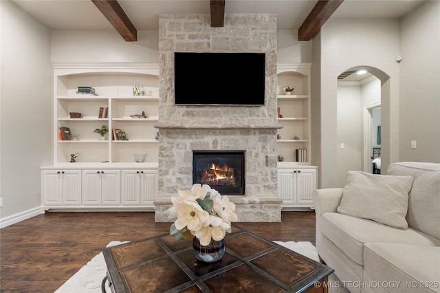 living room with dark wood-style floors, beam ceiling, a stone fireplace, arched walkways, and baseboards