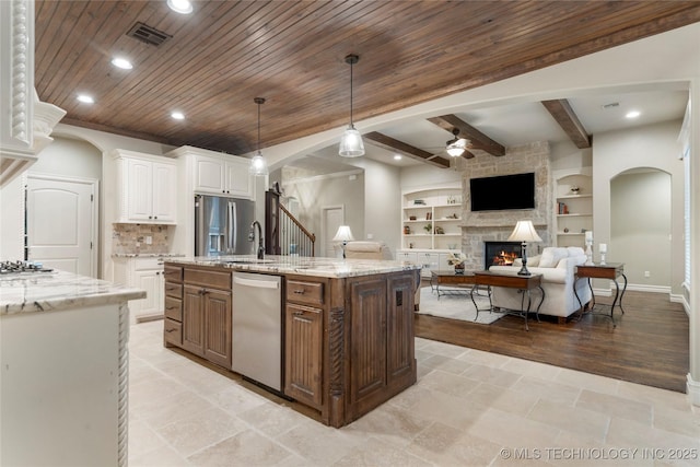 kitchen featuring arched walkways, appliances with stainless steel finishes, ceiling fan, white cabinets, and a stone fireplace
