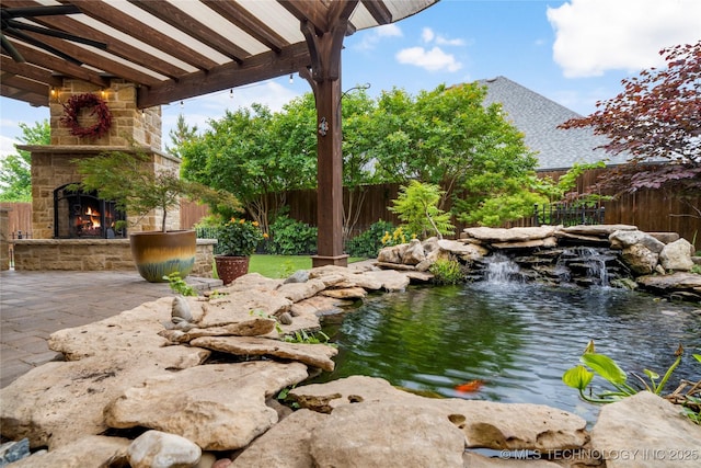 view of yard with an outdoor stone fireplace, fence, a small pond, and a patio area