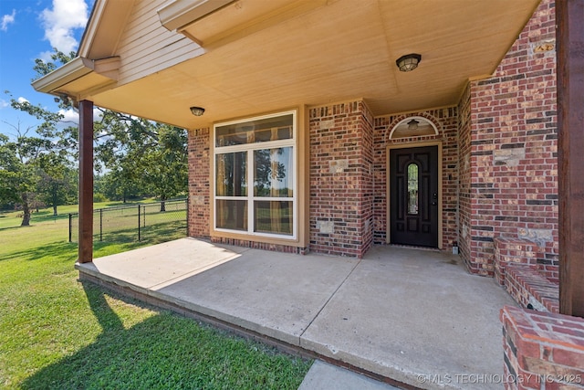 view of exterior entry with brick siding and a patio