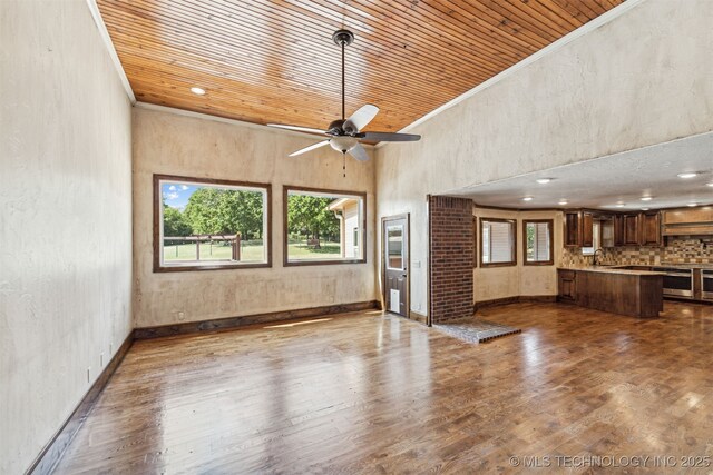 unfurnished living room featuring wood finished floors, wood ceiling, ceiling fan, a high ceiling, and ornamental molding