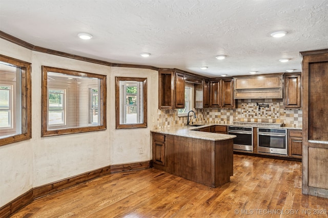 kitchen featuring oven, a sink, a peninsula, dark wood finished floors, and crown molding