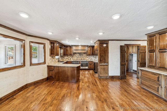 kitchen featuring a peninsula, ornamental molding, baseboards, dark wood-style floors, and a sink