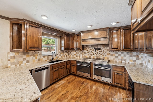 kitchen with appliances with stainless steel finishes, a sink, light stone counters, wood finished floors, and decorative backsplash