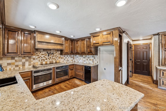 kitchen with oven, black electric stovetop, a sink, light stone countertops, and crown molding