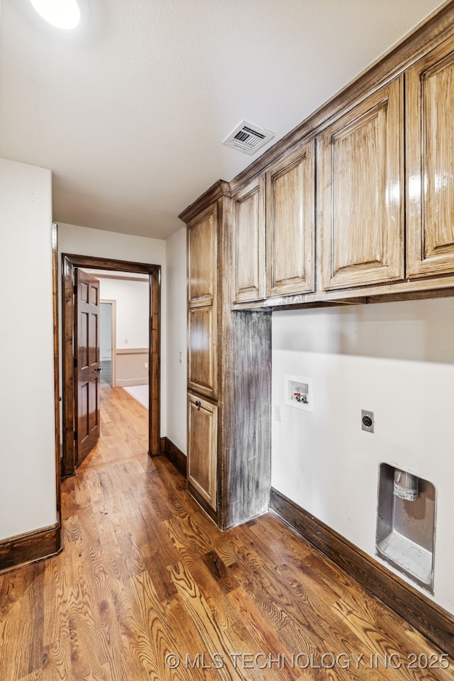 clothes washing area with cabinet space, hookup for a washing machine, hookup for an electric dryer, dark wood-type flooring, and baseboards
