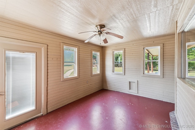 unfurnished room with concrete flooring, ceiling fan, and wooden walls