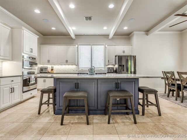 3661 S Lewis Ave, Tulsa, OK 74105 - kitchen with appliances with stainless steel finishes, beamed ceiling, white cabinetry, backsplash, and a center island