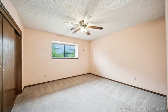 unfurnished bedroom featuring light colored carpet, a closet, baseboards, a ceiling fan, and a textured ceiling