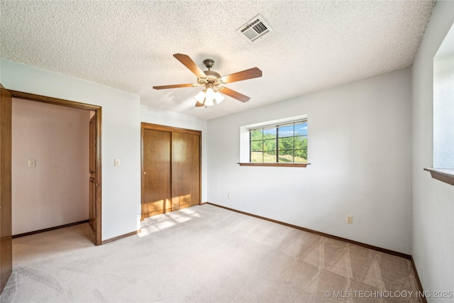 unfurnished bedroom with a closet, light colored carpet, baseboards, a ceiling fan, and a textured ceiling