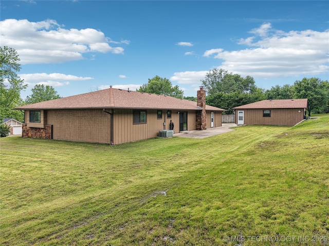 rear view of house with a chimney, a patio, central AC, a yard, and stone siding