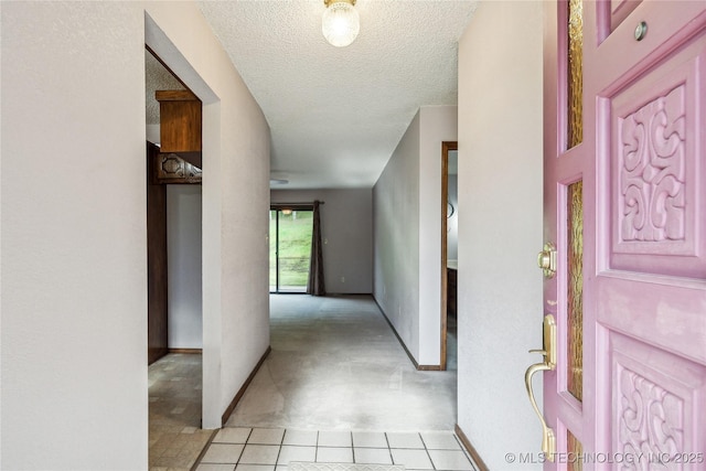 hallway featuring baseboards, a textured ceiling, and light tile patterned floors