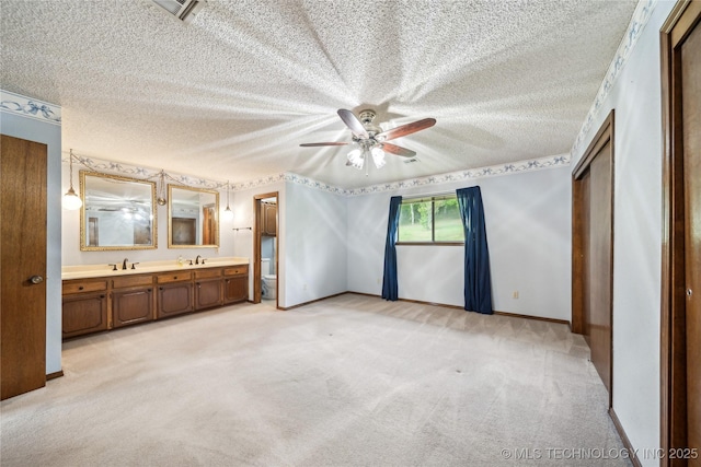 unfurnished bedroom featuring light carpet, a sink, ensuite bathroom, a textured ceiling, and baseboards