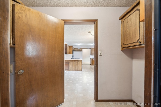 hallway with a textured ceiling, baseboards, and light flooring