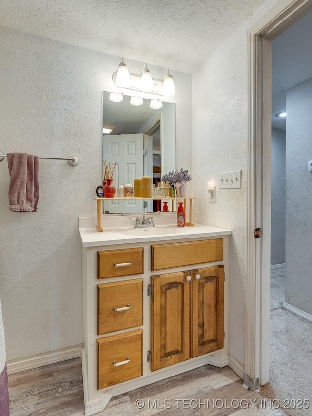 bathroom with a textured wall, vanity, baseboards, and wood finished floors