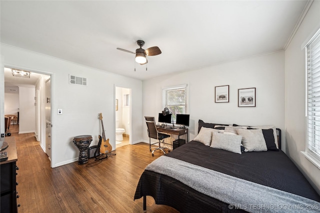 bedroom featuring wood finished floors, a ceiling fan, baseboards, ensuite bathroom, and ornamental molding