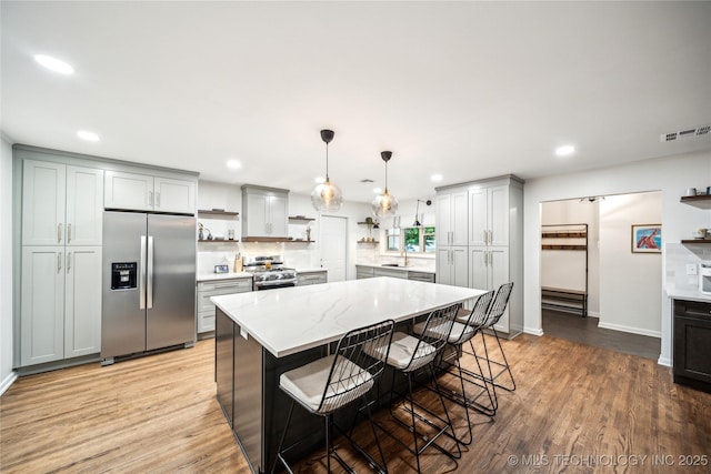 kitchen with stainless steel appliances, open shelves, a sink, light wood finished floors, and recessed lighting