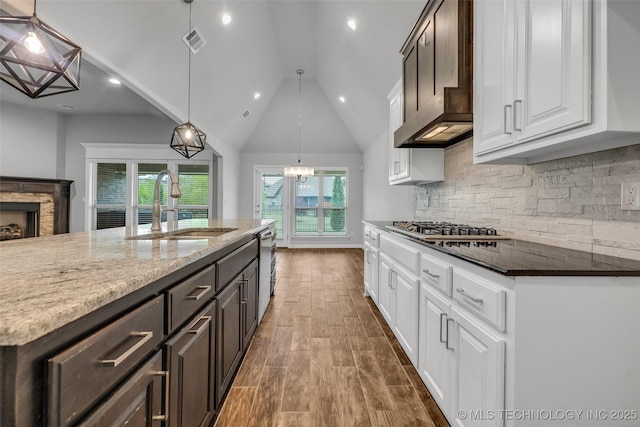 kitchen with a sink, stainless steel gas cooktop, white cabinetry, dark wood-type flooring, and vaulted ceiling