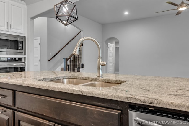 kitchen with a sink, stainless steel appliances, arched walkways, light stone counters, and recessed lighting