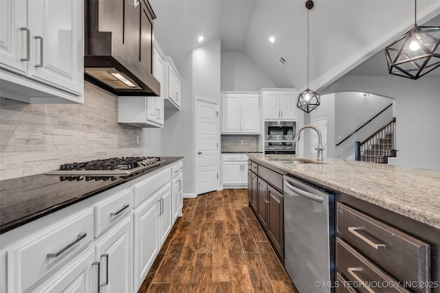 kitchen with appliances with stainless steel finishes, wall chimney exhaust hood, a sink, white cabinets, and dark brown cabinetry