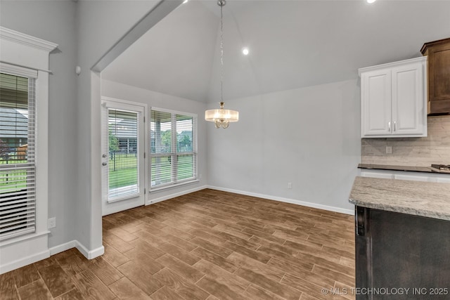 unfurnished dining area featuring lofted ceiling, a chandelier, baseboards, and wood finished floors