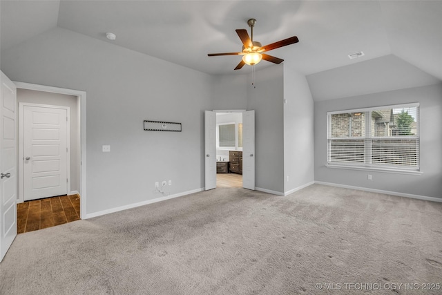 unfurnished bedroom featuring vaulted ceiling, carpet floors, baseboards, ensuite bathroom, and ceiling fan