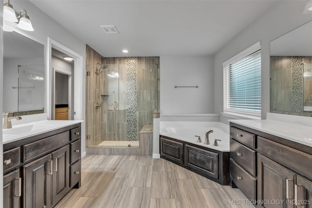 bathroom featuring a stall shower, a bath, recessed lighting, and two vanities