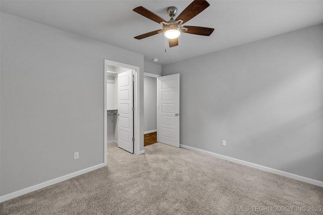 unfurnished bedroom with carpet, baseboards, a spacious closet, a closet, and ceiling fan