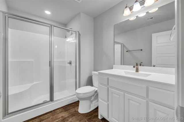 bathroom featuring wood finished floors, a shower stall, toilet, vanity, and recessed lighting