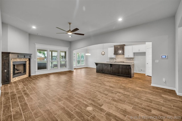 unfurnished living room featuring ceiling fan, baseboards, a tiled fireplace, recessed lighting, and wood finished floors