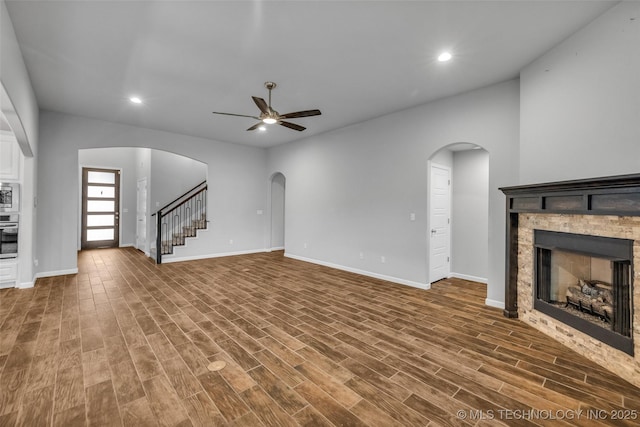 unfurnished living room featuring ceiling fan, a stone fireplace, baseboards, recessed lighting, and wood finished floors