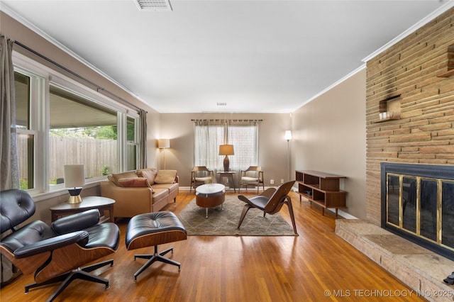 living room with wood finished floors, healthy amount of natural light, ornamental molding, and a fireplace