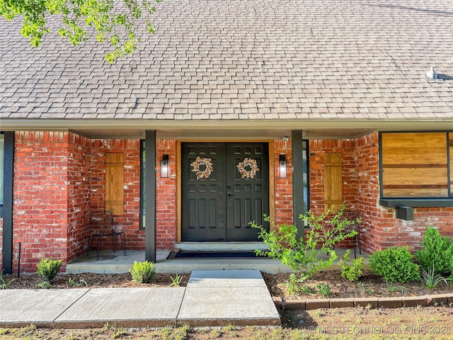 entrance to property featuring brick siding and roof with shingles